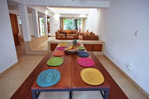 Un comedor con una larga mesa de madera, individuales coloridos y una isla central con frutas.