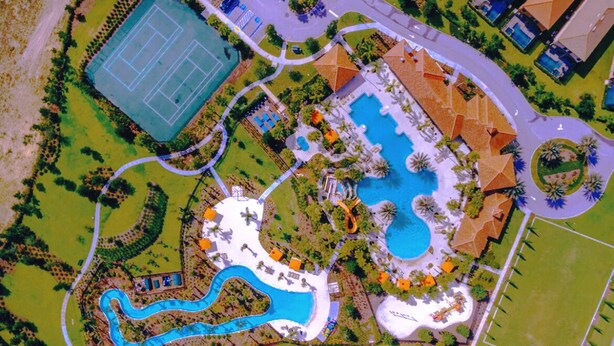 Vue aérienne d’un complexe hôtelier doté d’une grande piscine centrale, d’un court de tennis et d’une installation aquatique sinueuse.