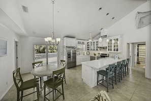 Una cocina amplia con una isla grande, armarios blancos y un comedor con sillas de madera.