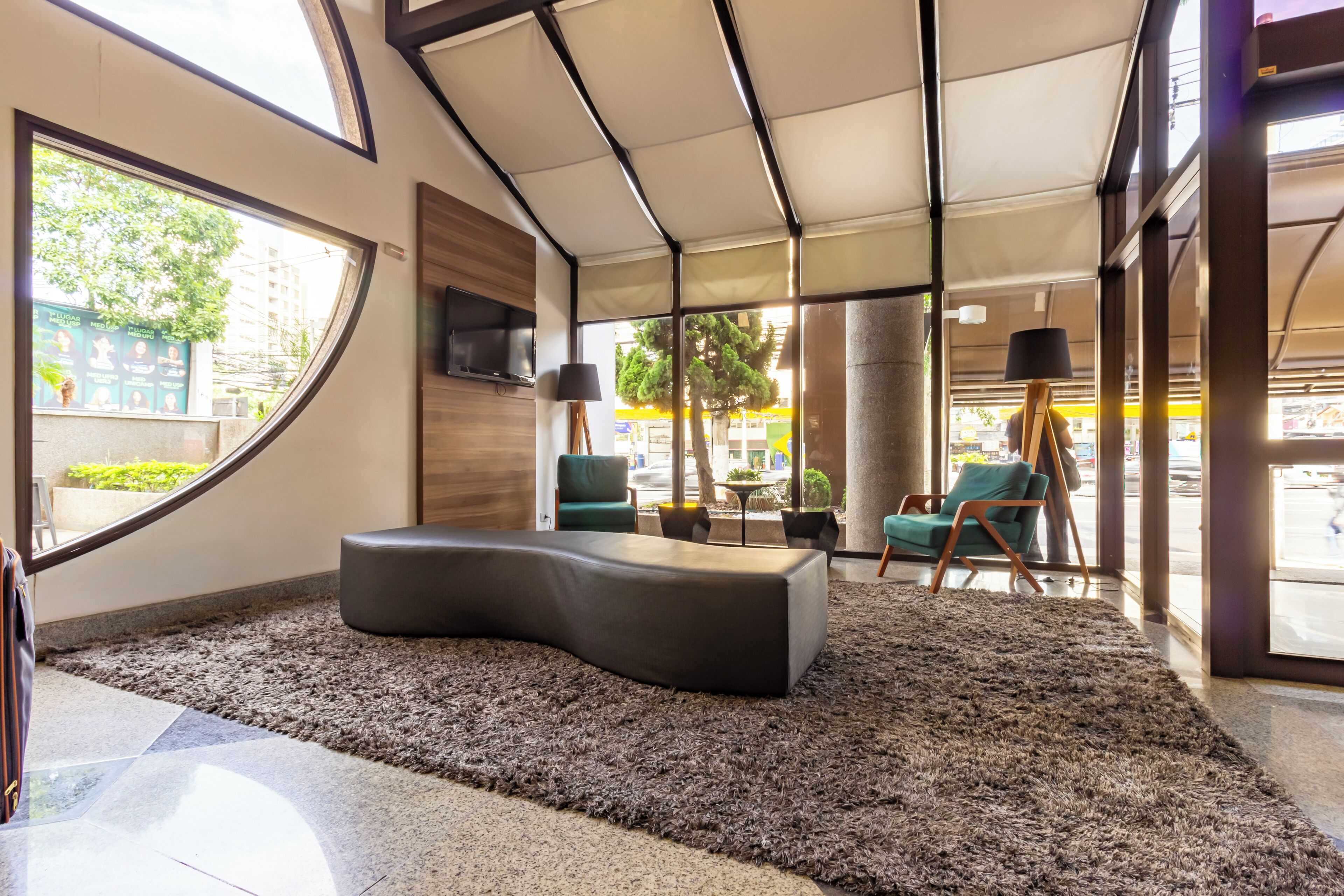 Un moderno vestíbulo de hotel con una zona de estar curva, un amplio ventanal con vistas a la calle y un techo con un diseño geométrico único.
