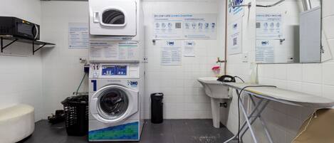 A public restroom with a washing machine, a sink, a mirror, and informational posters on the wall.