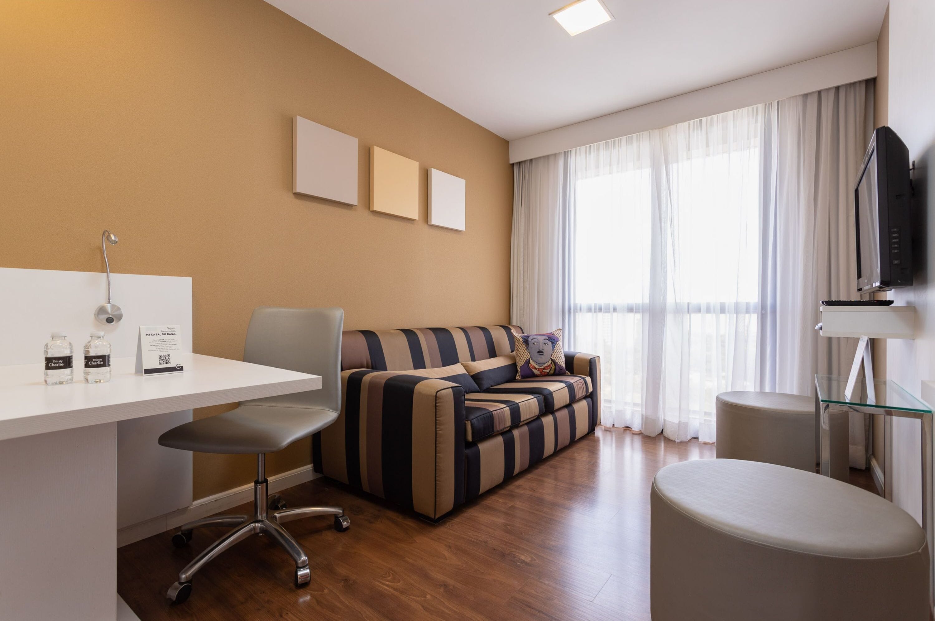 A modern living room with a sofa, a glass table, a TV, and a desk with a chair.