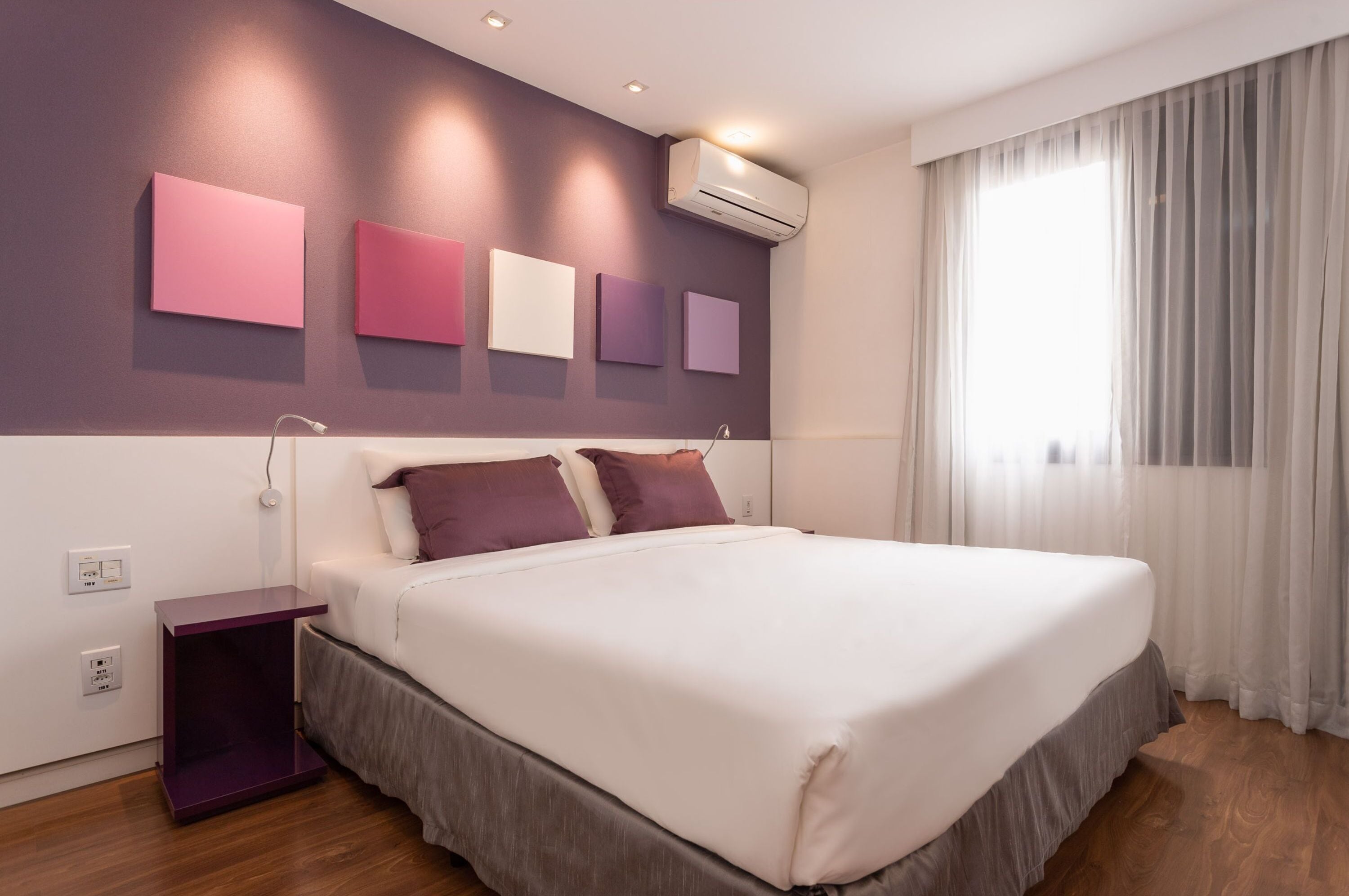 Quarto moderno com uma cama grande, uma mesa de cabeceira e ar condicionado fixado na parede.