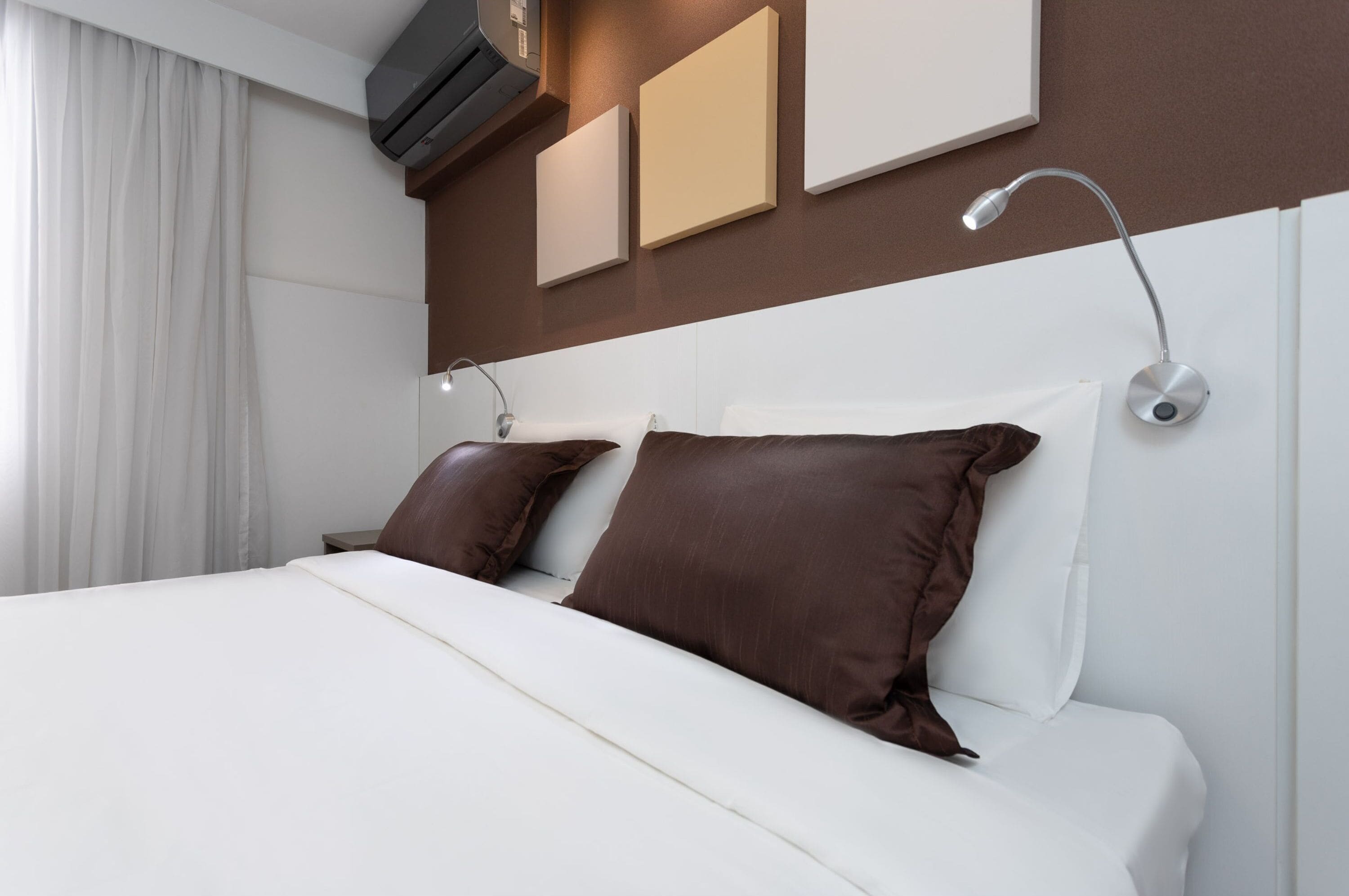 Een moderne hotelkamer met een groot bed, twee kussens, een nachtkastje, een wandlamp en een raam met gordijnen.
