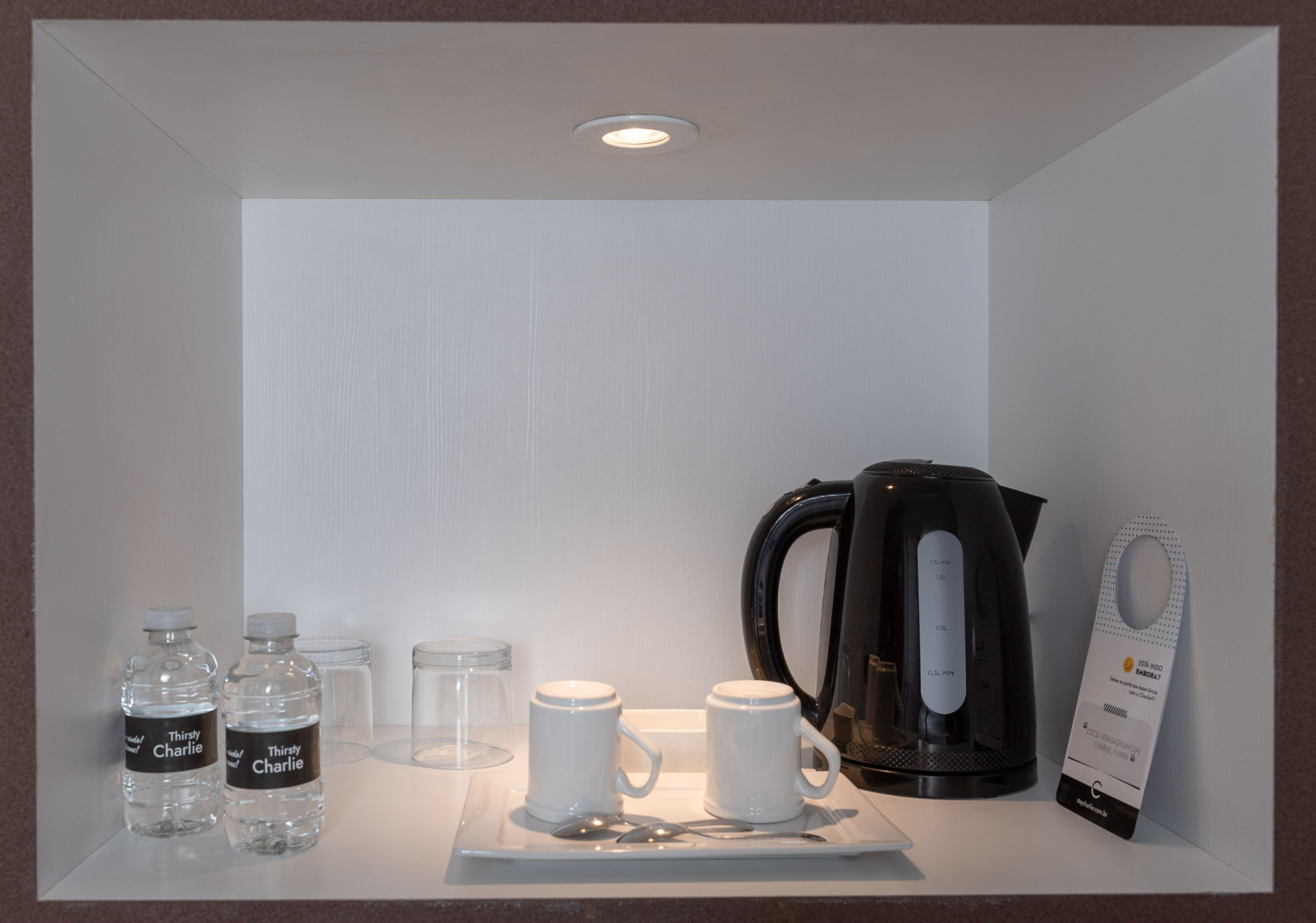 De minibar van een hotelkamer, met waterflessen, een koffiezetapparaat en een lepel.