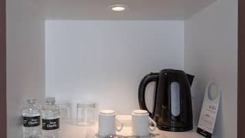 De minibar van een hotelkamer, met waterflessen, een koffiezetapparaat en een lepel.