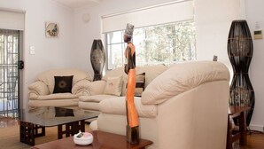 A spacious living room with a high ceiling, a ceiling fan, a large window, a beige sofa, a wooden coffee table, and a decorative sculpture. - Amazing, secluded twenty-five acre property - yet close to everything you need! (Lovedale)