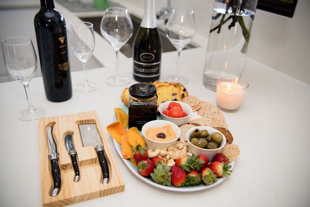 Ein Tisch gedeckt mit Weinflaschen, Gläsern, einer Kerze sowie verschiedenen Snacks und Früchten.