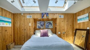 Une chambre à coucher avec un grand lit, des murs en bois, des fenêtres de toit et des œuvres d’art.