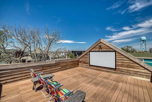 A wooden deck with a built-in screen, colorful lounge chairs, and a view of a swimming pool and water tower.