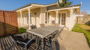 A covered patio with a table and chairs, a wooden fence, and a satellite dish. - Relax on Rata Cottage 1 (Twizel)