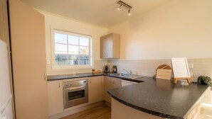 A compact kitchen with a built-in oven, a sink, and a window. - Relax on Rata Cottage 1 (Twizel)