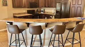 Una cocina con armarios de madera oscura, encimera de granito, refrigerador negro y cuatro taburetes de bar.
