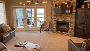 Una sala de estar con chimenea de piedra, sofás de cuero, una mesa de centro y un televisor montado en la pared.