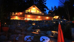 A modern house with a large balcony, stone walls, and a well-lit interior.