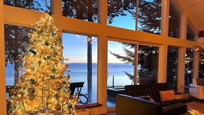 A spacious living room with a large Christmas tree, a view of the sea through large windows, and modern furniture.