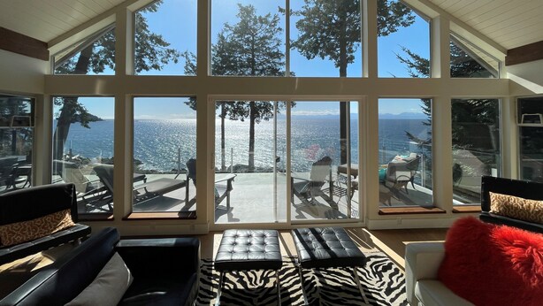 A sunlit room with large windows offering a view of the sea and trees.