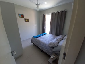Un dormitorio pequeño y ordenado con cama, mesita de noche y ventilador de techo.