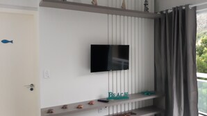 Quarto com televisão na parede, porta com puxador e janela com cortina.