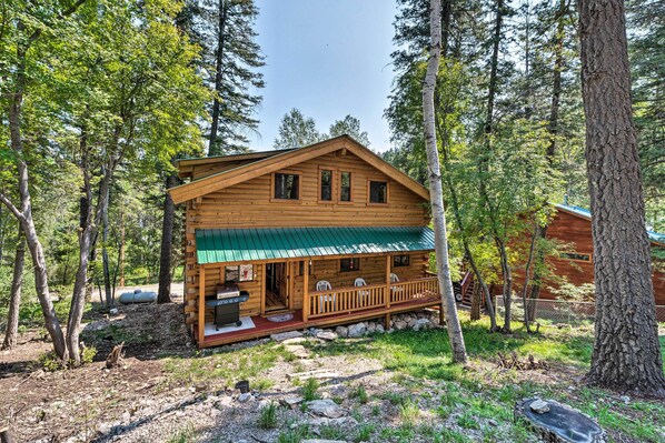 A wooden cabin with a porch, surrounded by trees.