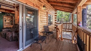 Una cabaña de madera con un porche cubierto, puertas de vidrio correderas y una zona de estar con sillas y una mesa.