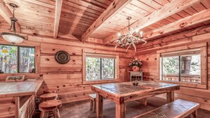 Interior de una cabaña de madera con una gran mesa de comedor, bancos y una araña.