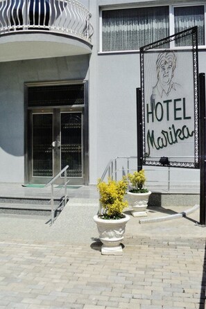 Ein Hotel Eingang mit einem Schild, auf dem 'HOTEL Marika' steht, einem Metallgitter und Blumentöpfen.
