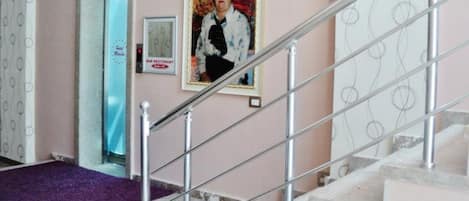 A staircase with a metal handrail, a purple carpeted landing, and a wall with a framed picture and a sign.