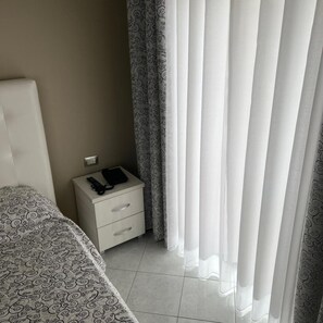 Ein Schlafzimmer mit einem Bett, einem Nachttisch mit Telefon und Buch sowie einem Fenster mit Vorhängen.