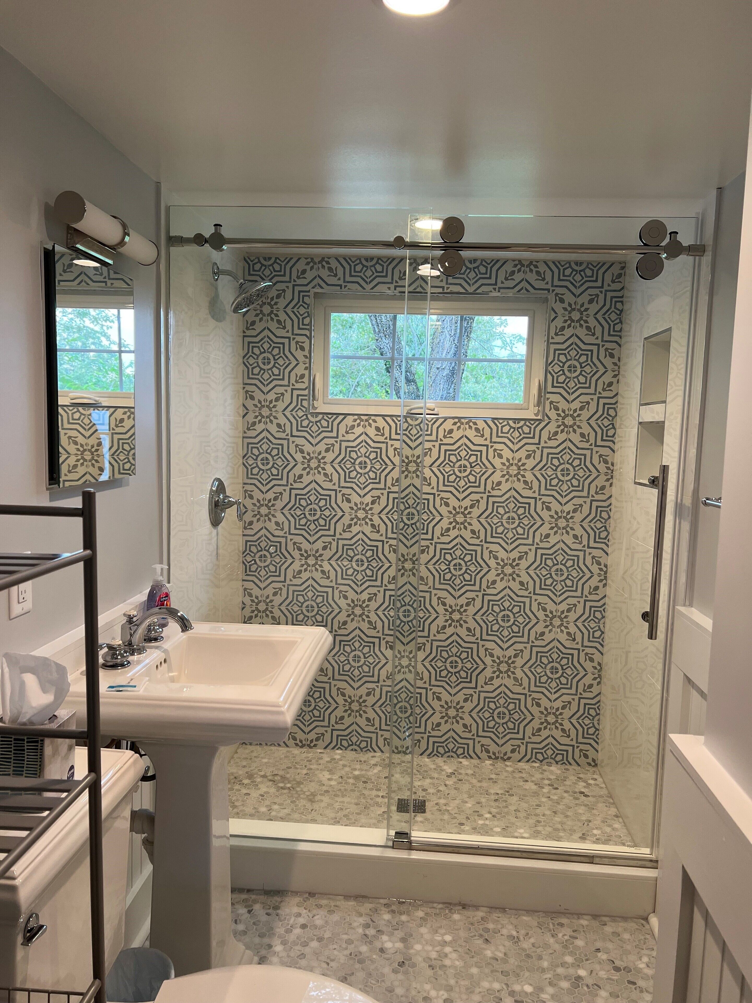 A bathroom with a shower, a sink, and a window.