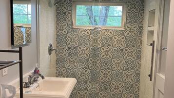 A bathroom with a shower, a sink, and a window.