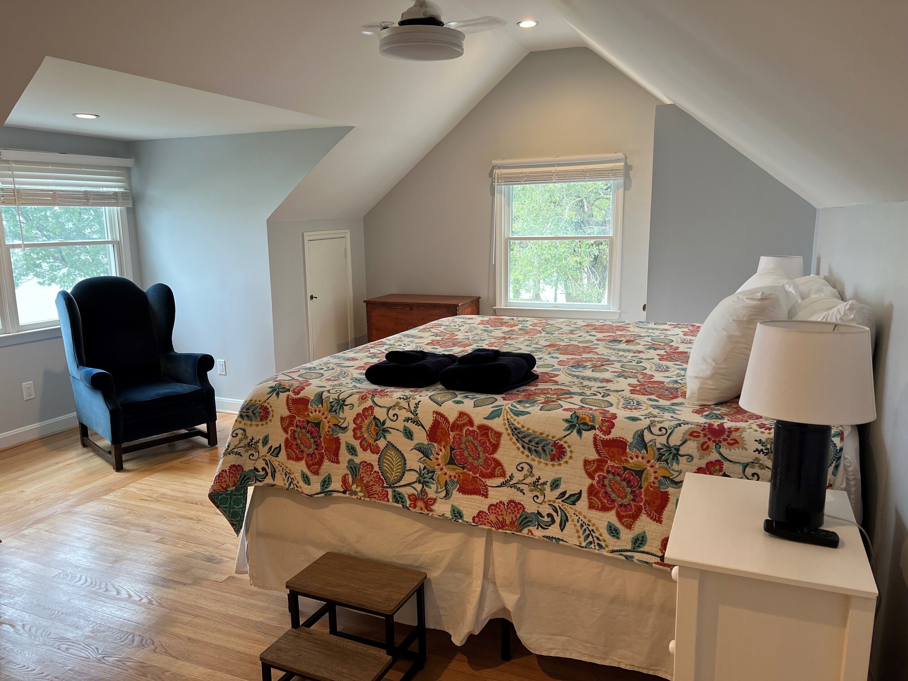 Une chambre à coucher avec un grand lit, une chaise, une petite table et une lampe.