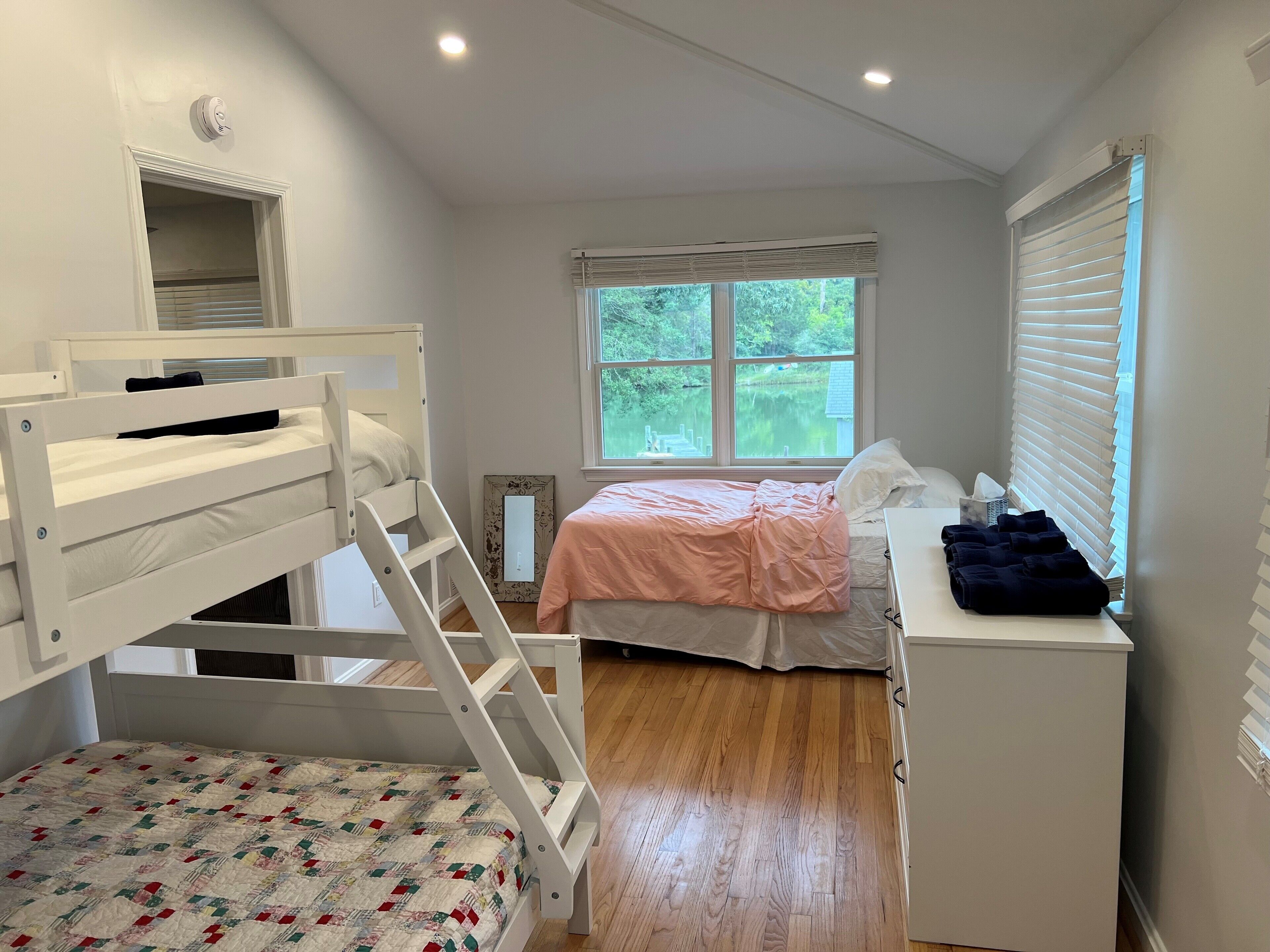 A bedroom with bunk beds, a single bed, a dresser, and a window with a view of greenery.