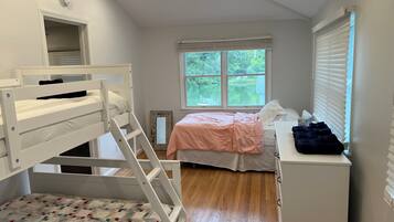 A bedroom with bunk beds, a single bed, a dresser, and a window with a view of greenery.