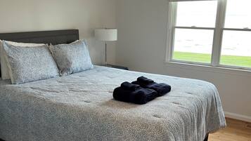 Een slaapkamer met een bed, een plafondventilator, een nachtkastje, een lamp en een raam met uitzicht.