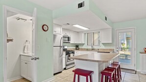 A kitchen with white cabinets, a stainless steel refrigerator, a microwave, and a stove. There are three red bar stools at the island.
