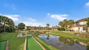 A golf course with a water hazard, palm trees, and residential-style buildings.