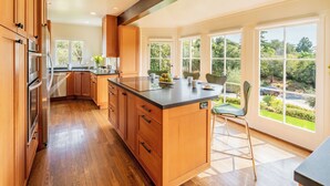 A modern kitchen with wooden cabinets, a central island, and large windows offering a view of the garden. - Stunning, Private Home With Pool, Hot Tub, and Mountain Views! (Santa Barbara)