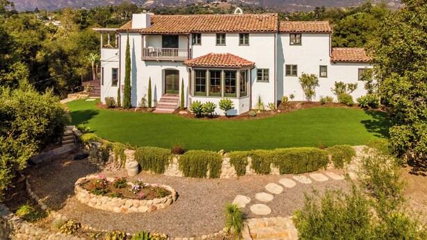 A two-story house with a white exterior and red-tiled roof, surrounded by a well-maintained garden and a mountain backdrop. - Stunning, Private Home With Pool, Hot Tub, and Mountain Views! (Santa Barbara)