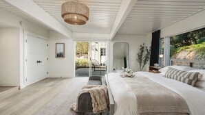 Une chambre à coucher moderne avec un grand lit, un banc et une vue sur l’extérieur.