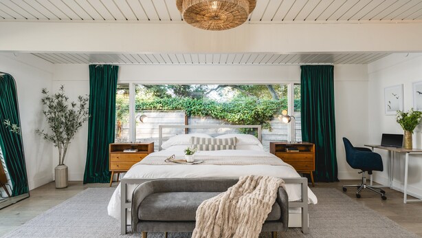 Une chambre moderne avec un grand lit, des tables de chevet, un bureau et une vue sur la verdure.