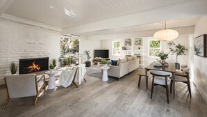 Un salon moderne avec une cheminée, des murs en briques blanches, un plancher en bois, un canapé, une table à manger et un téléviseur.