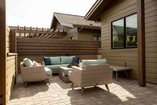A covered outdoor patio with wicker furniture, a wooden pergola, and a view of a house in the background. - 24-hr staff ~ resort pool ~ garage ~ wifi ~ W/D ~ fireplace ~ concert shuttle 🎵 (Bend)