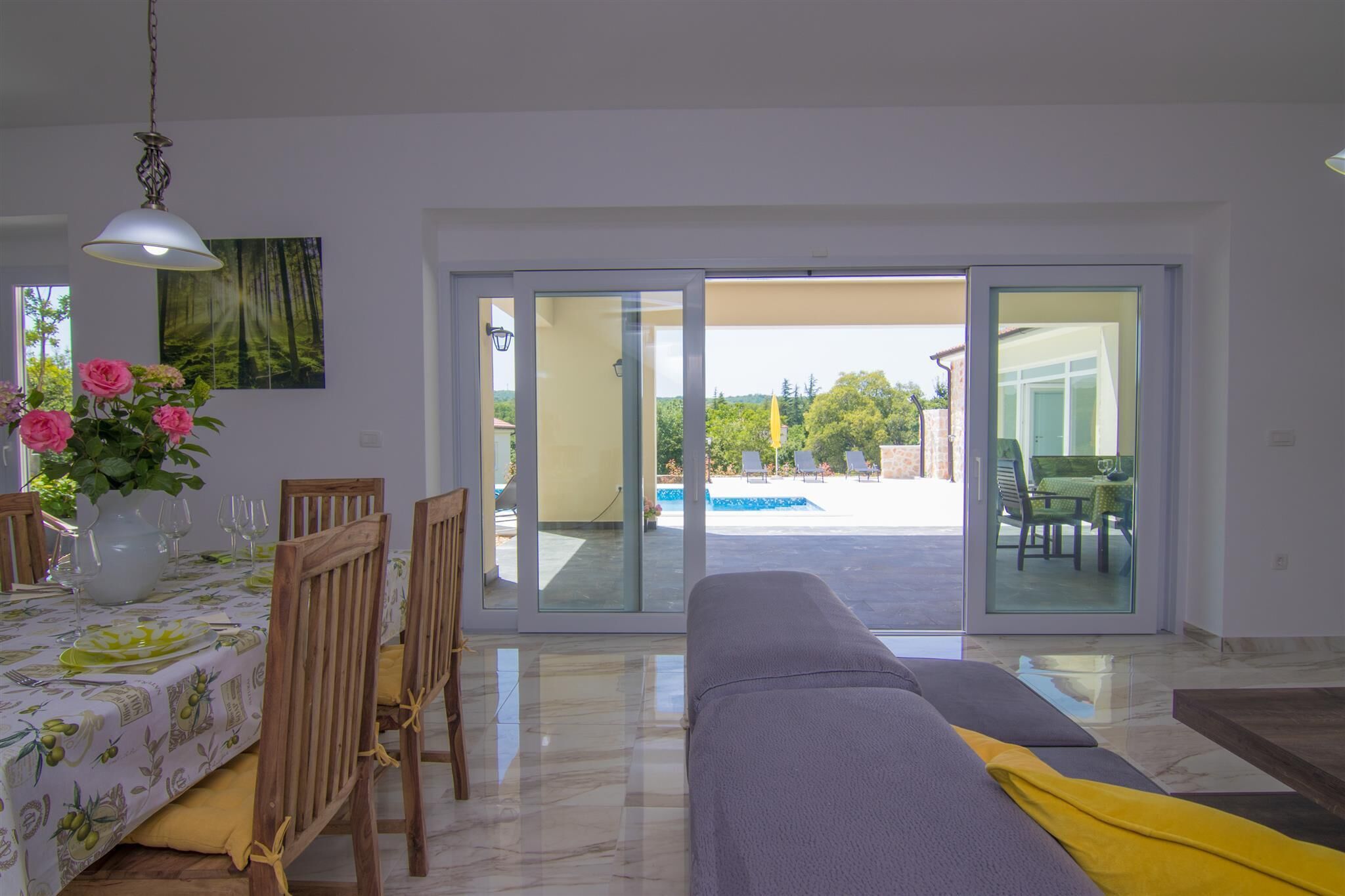 Un coin repas avec une table dressée pour quatre personnes, un canapé et une vue sur une piscine et un espace de détente extérieur.