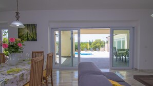 A dining area with a table set for four, a sofa, and a view of a swimming pool and outdoor seating. - Villa Cedar with large swimming pool and summer kitchen (Gostinjac (Krk))