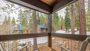 A wooden deck with a view of a building surrounded by tall trees.