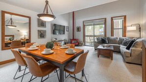 A spacious living room with a wooden dining table, comfortable seating, a fireplace, and large windows.