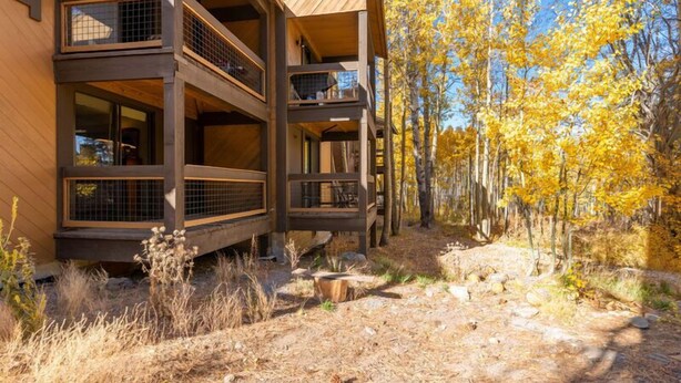 A multi-story wooden cabin with balconies, surrounded by a forest with autumn foliage.