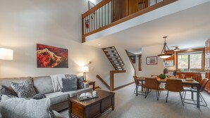 A spacious living room with a sofa, coffee table, and a dining area with chairs and a table. A staircase leads to an upper level.