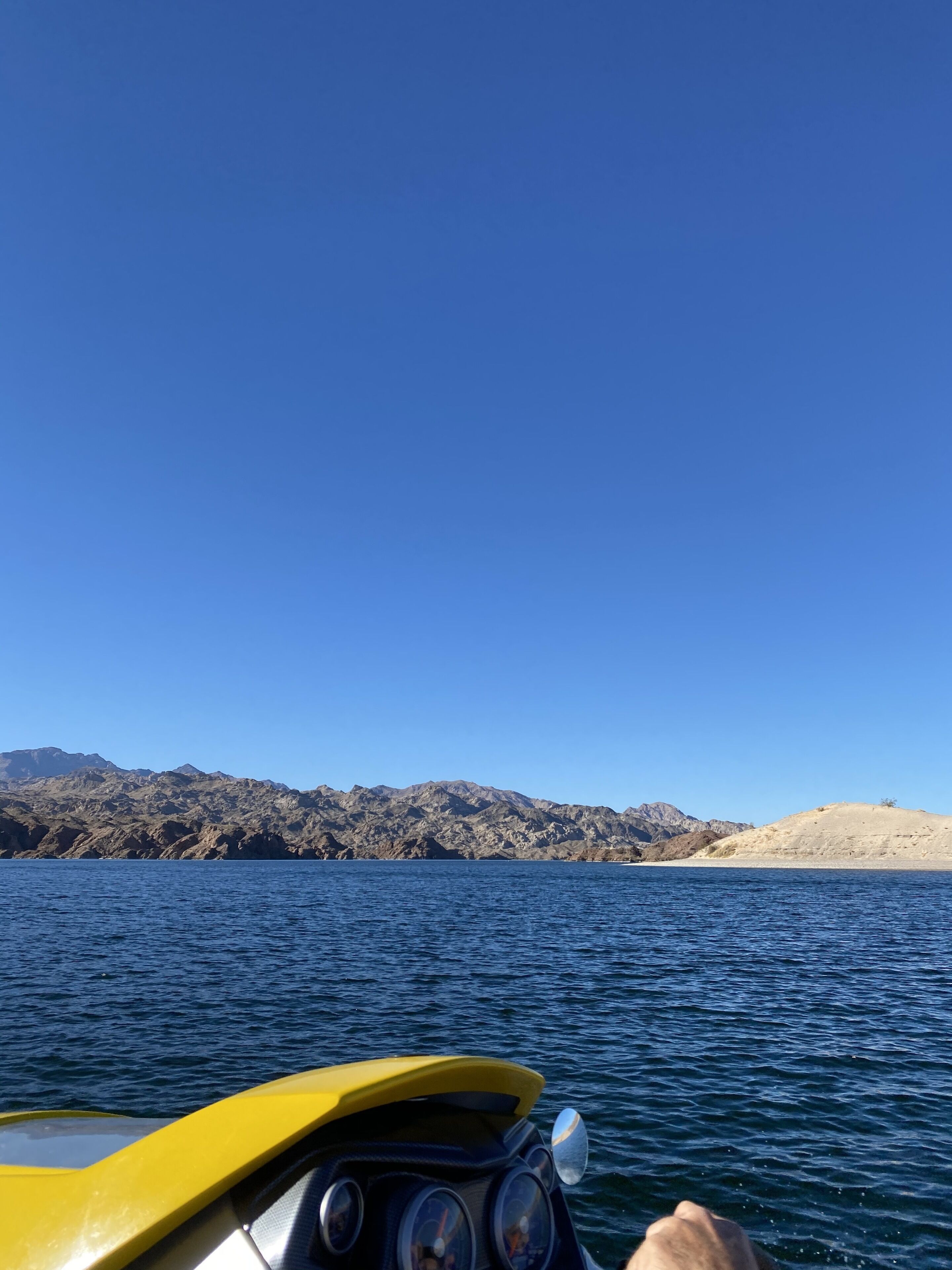 Un bateau à la proue jaune, un ciel bleu azur et un paysage montagneux en arrière-plan.